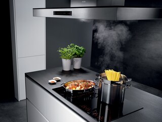 Alimentos cocinándose en una placa de inducción AEG mientras una campana de cocina AEG extrae el exceso de vapor