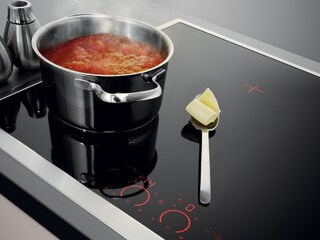 Sartén en la que se hace una salsa a fuego lento y, a su lado, una cuchara de mantequilla sobre la superficie de la encimera