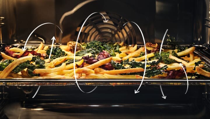 Patatas fritas y verduras cocinándose en un horno.