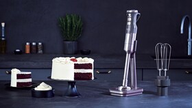 La batidora de mano con un pastel de chocolate glaseado