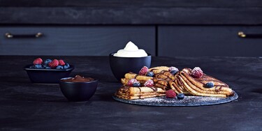 Montones de tortitas dobladas espolvoreadas con salsa de chocolate y recubiertas de frutos del bosque