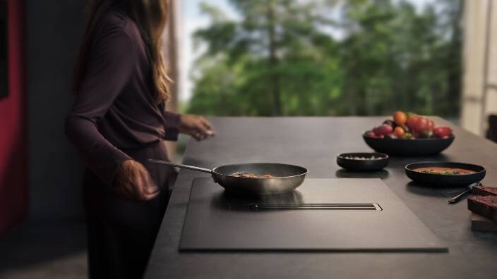 A lady cooking food in a pan on AEG SaphireMatt